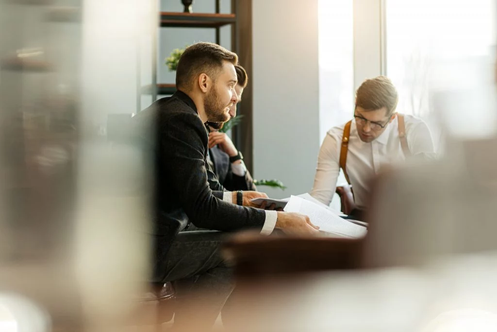 Mehrere Personen besprechen Unterlagen in einem hellen Büro, gesehen durch eine unscharfe Glasfläche in ruhiger, professioneller Atmosphäre.