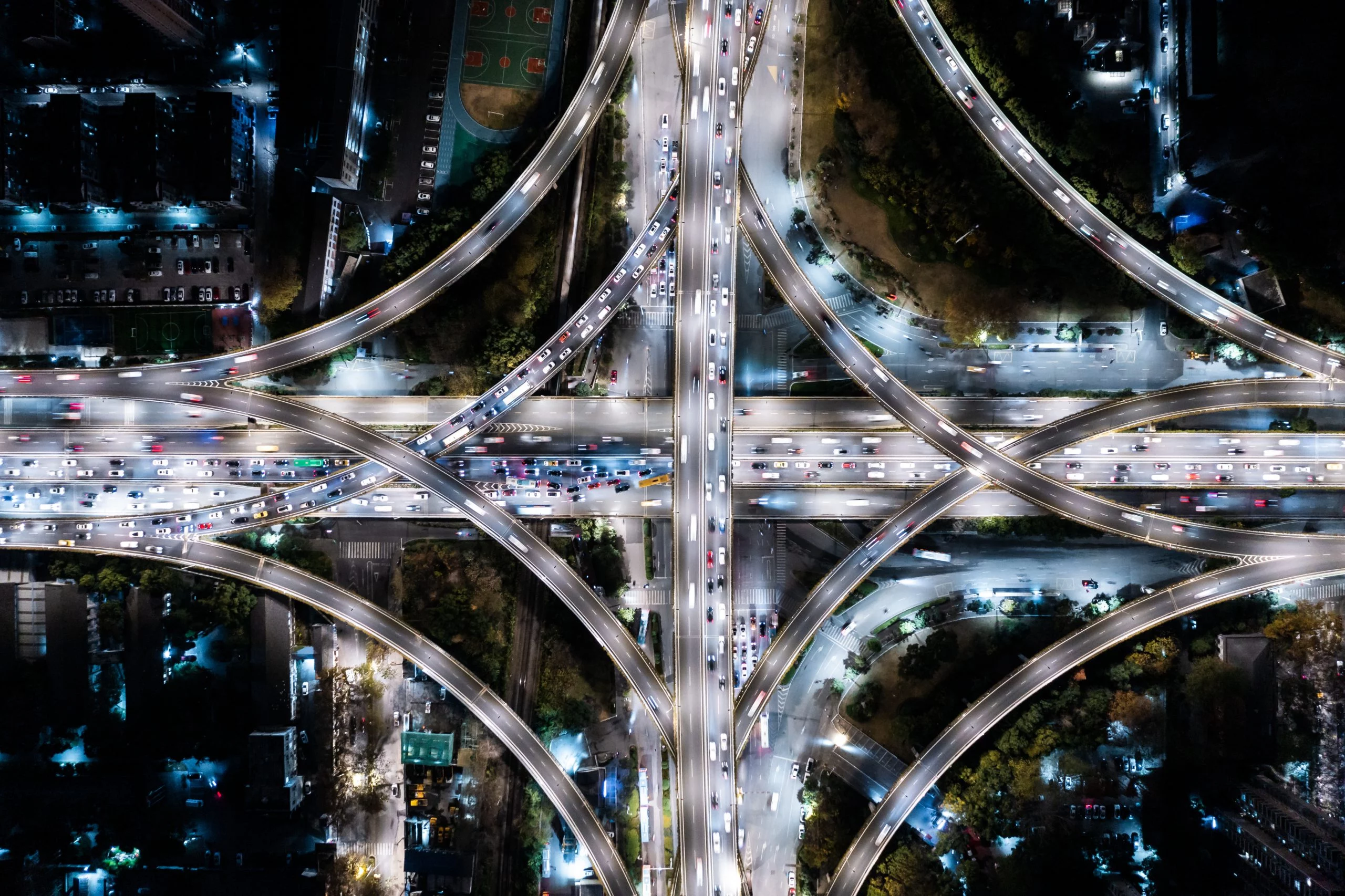 Luftaufnahme eines beleuchteten Autobahnkreuzes bei Nacht mit dichtem Verkehr auf mehreren Fahrspuren.